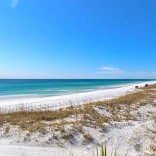White sand beach and grassy dunes beside turquoise water, with beachfront condo buildings along the shoreline.